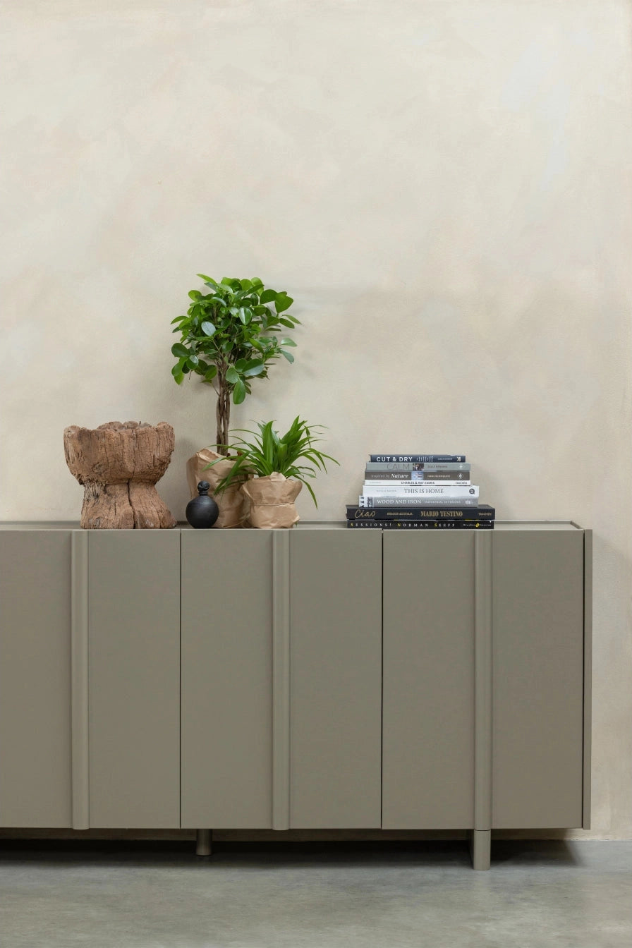 Vooraanzicht van het Basu dressoir van grenenhout in de kleur mud, met boeken en een plantje als accessoires