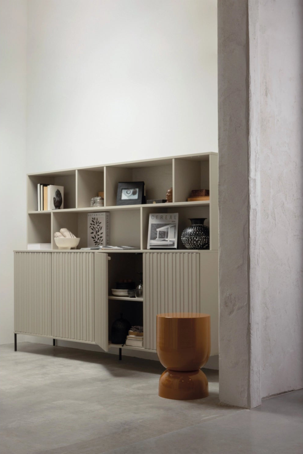 New Gravure wandkast in grenen dust, gevuld met accessoires, met een oranje Hekla bijzettafel ervoor in een sfeervolle setting
